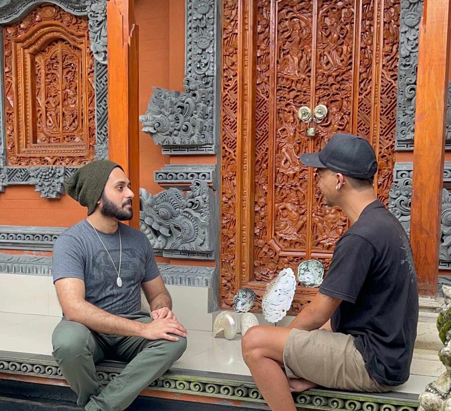 Two men sitting on a stone bench in front of a ornate wooden door.