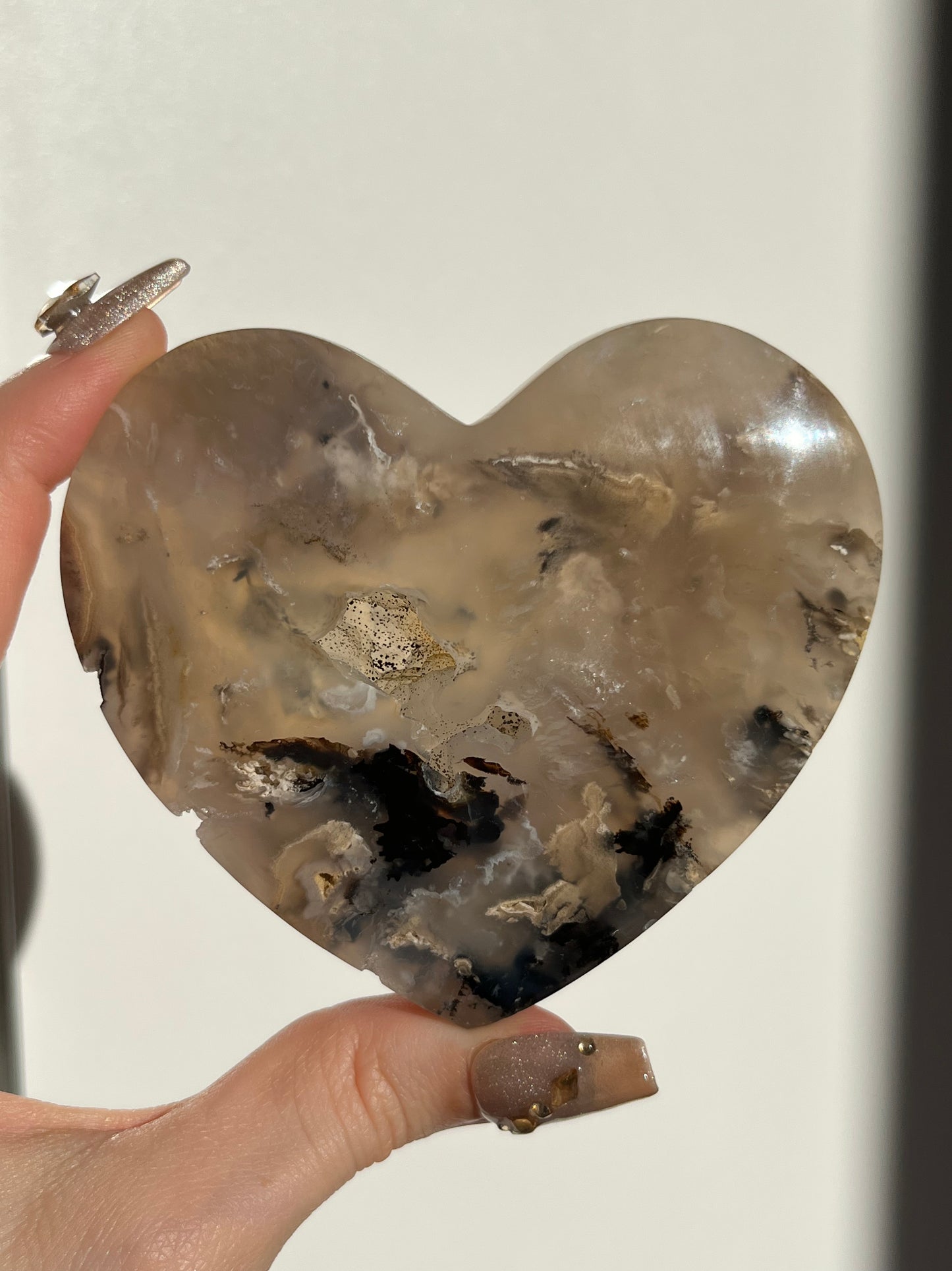 Heart-shaped crystal held by a hand against a neutral background