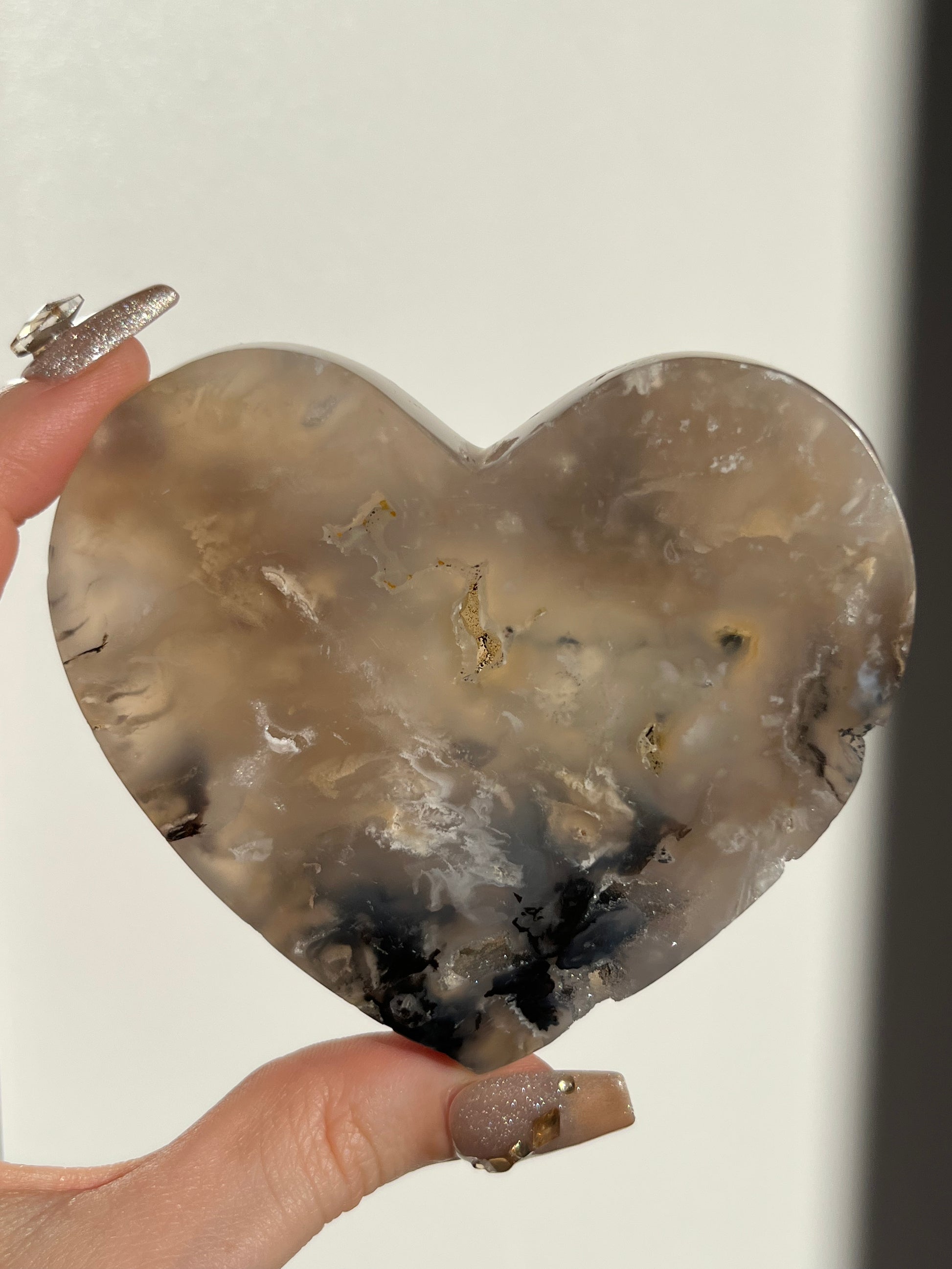 Heart-shaped stone held by a hand with glittery nail polish on a light background
